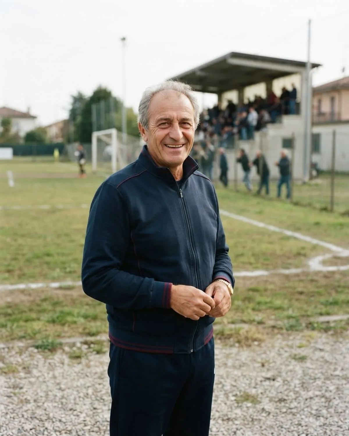 Presidente di una società calcistica in tuta sociale a bordo campo, con la tribuna alle spalle